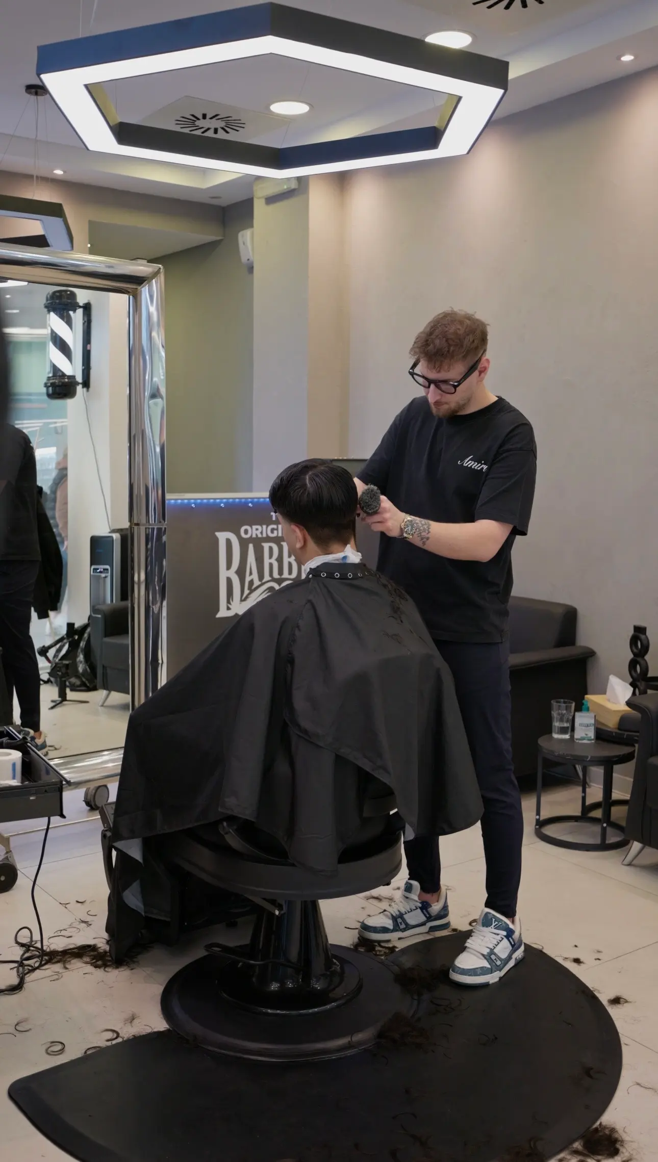 Barber stříhá klienta strojkem u zrcadla s nápisem Original Barber